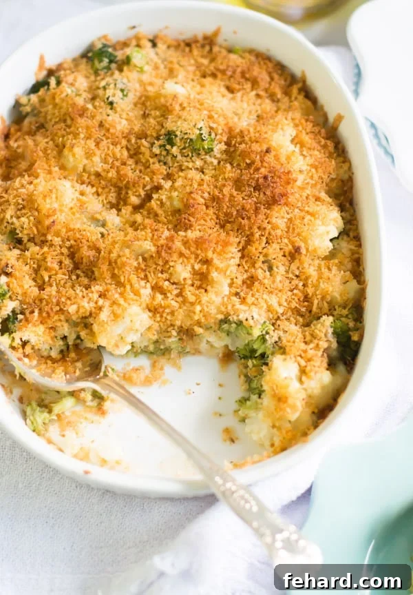 Serving up a warm, comforting portion of cheesy vegetable casserole. A casserole dish of cheesy broccoli cauliflower bake with a serving spooned out, revealing the creamy interior and golden crispy topping.