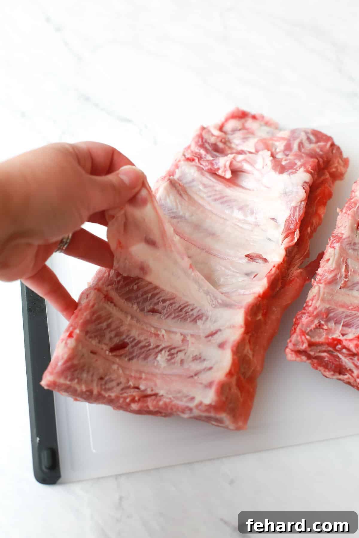 Effortlessly Tender Instant Pot Ribs 3 Detail shot of a hand removing the thin membrane from the back of a rack of baby back ribs.