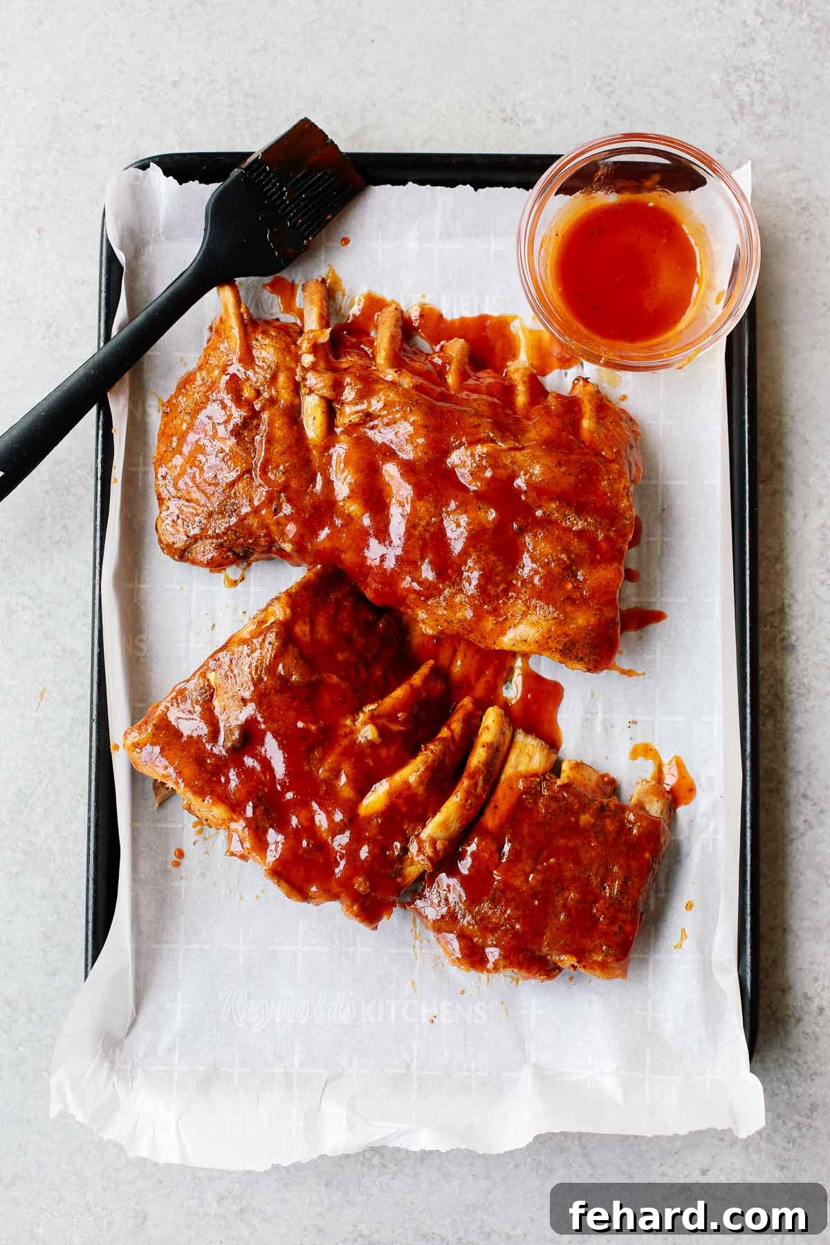 Effortlessly Tender Instant Pot Ribs 8 Cooked ribs on a sheet pan, generously brushed with barbecue sauce, ready for broiling.