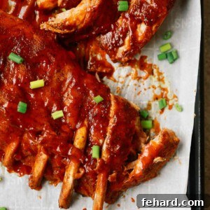 A close up of ribs on a baking sheet, glistening with sauce