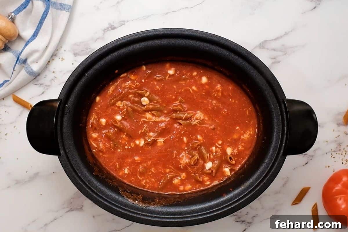 Crockpot Baked Ziti with Pasta and Cheese Uncooked ziti, cottage cheese, and mozzarella being mixed into spaghetti sauce in a slow cooker.