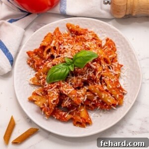Crockpot Pasta dished out on white plate topped with parmesan and basil.