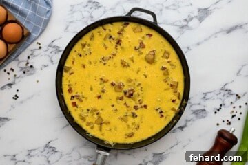 Heat-safe skillet with egg mixture, potatoes, bacon, and cheese before baking.