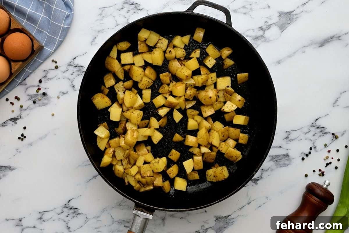 Sautéed potato cubes in a cast-iron skillet, seasoned with salt and pepper, ready for the egg mixture.