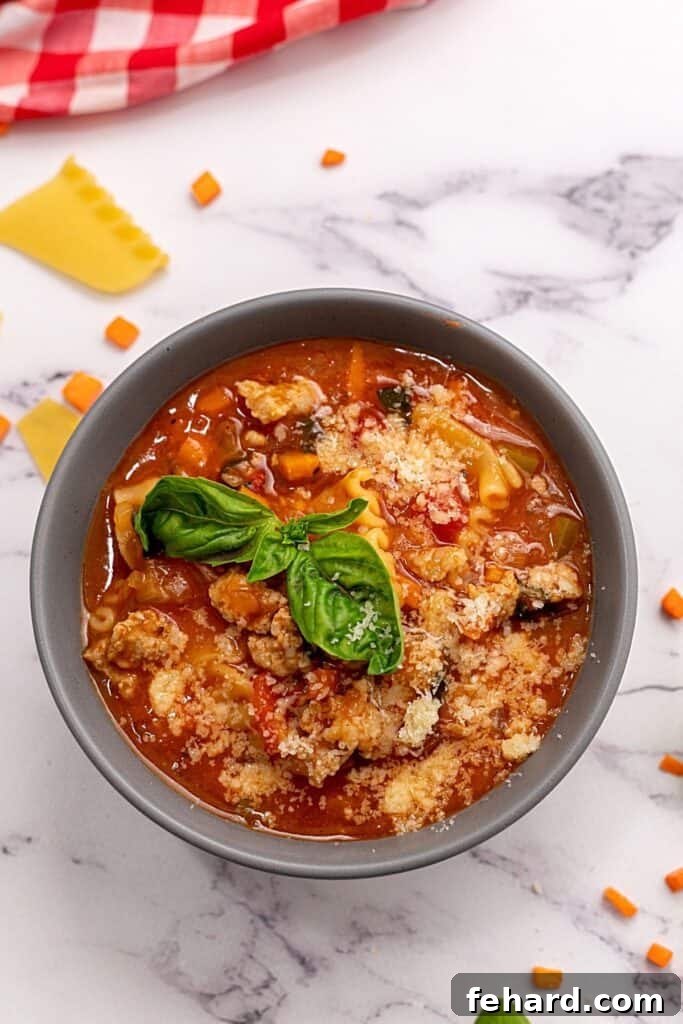A steaming bowl of homemade Lasagna Soup in a gray bowl, garnished with fresh basil leaves and melted cheese.