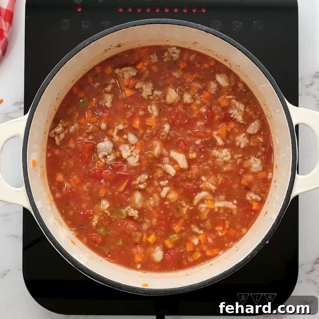 Close-up shot of ingredients for lasagna soup simmering in a large Dutch oven pan, showcasing the rich tomato broth.