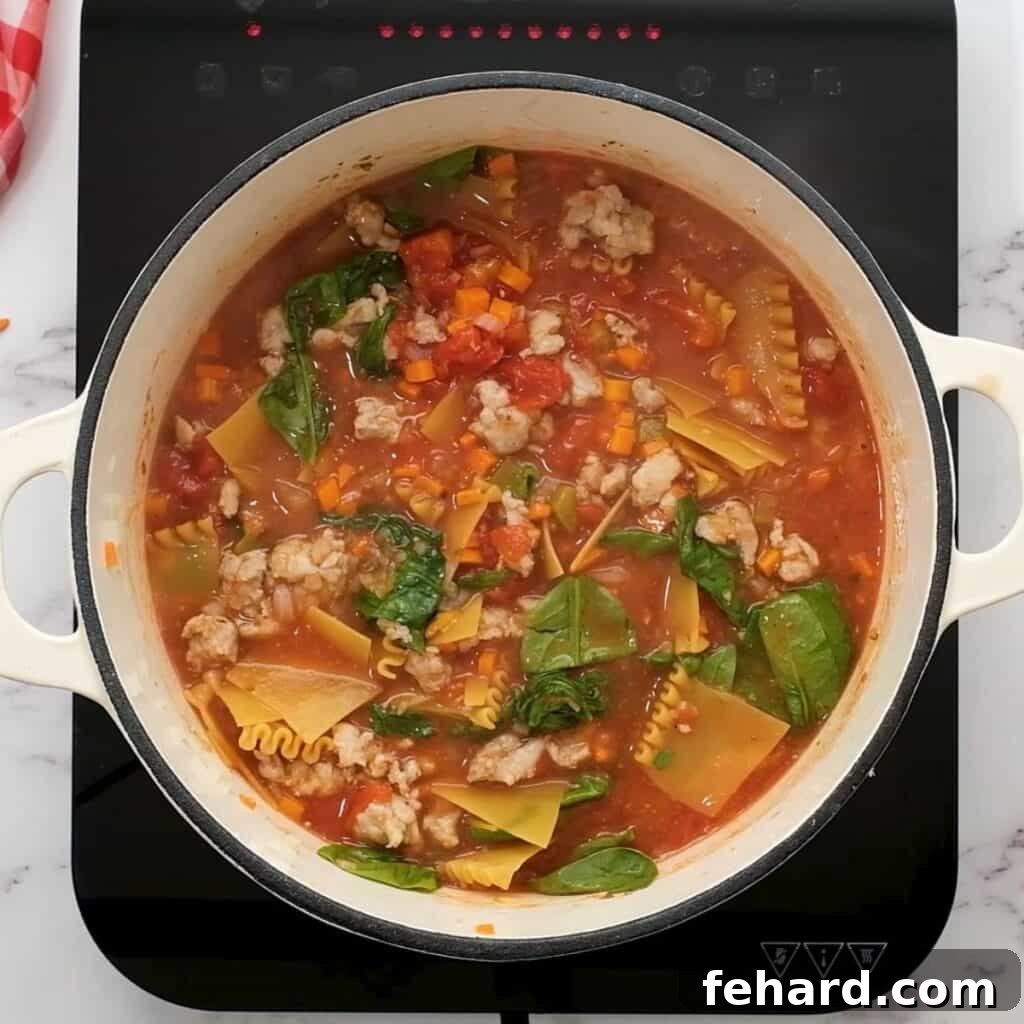 A large pot of freshly cooked Lasagna Soup with vibrant green spinach stirred in, ready to be served.