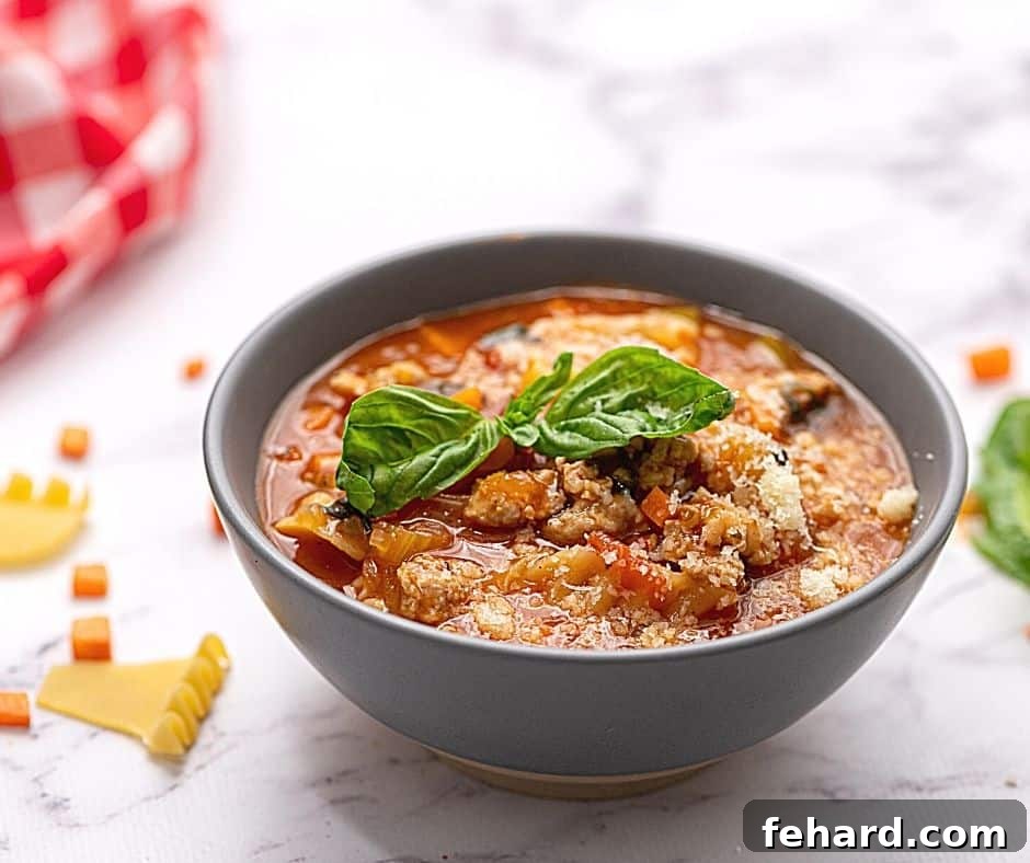 A beautifully garnished bowl of Lasagna Soup, topped with melted mozzarella, grated Parmesan, and fresh basil leaves.