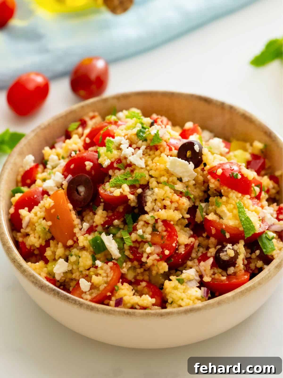 A vibrant Cold Couscous Salad, generously garnished with olives, grape tomatoes, and crumbled feta cheese, showcasing its Mediterranean appeal.