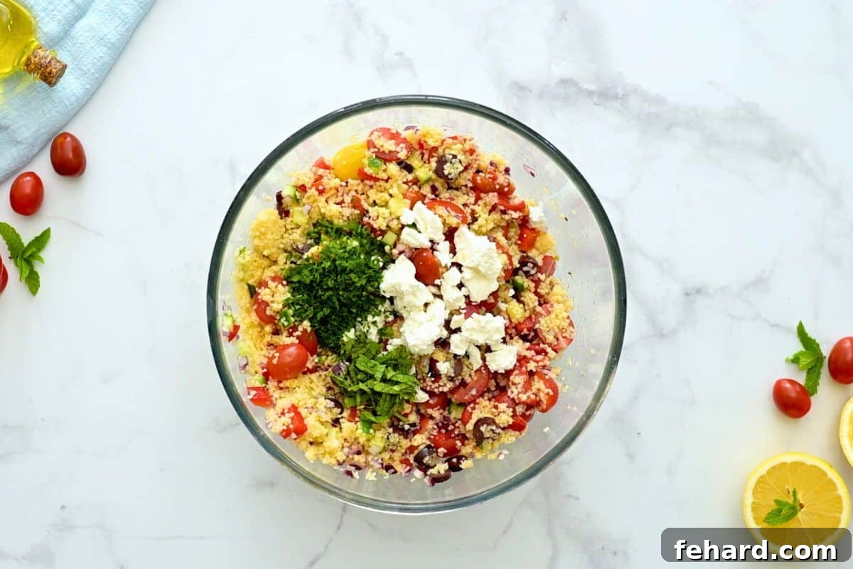 A beautifully presented bowl of Cold Couscous Salad, garnished with fresh mint, parsley, and crumbled feta cheese, ready to serve.