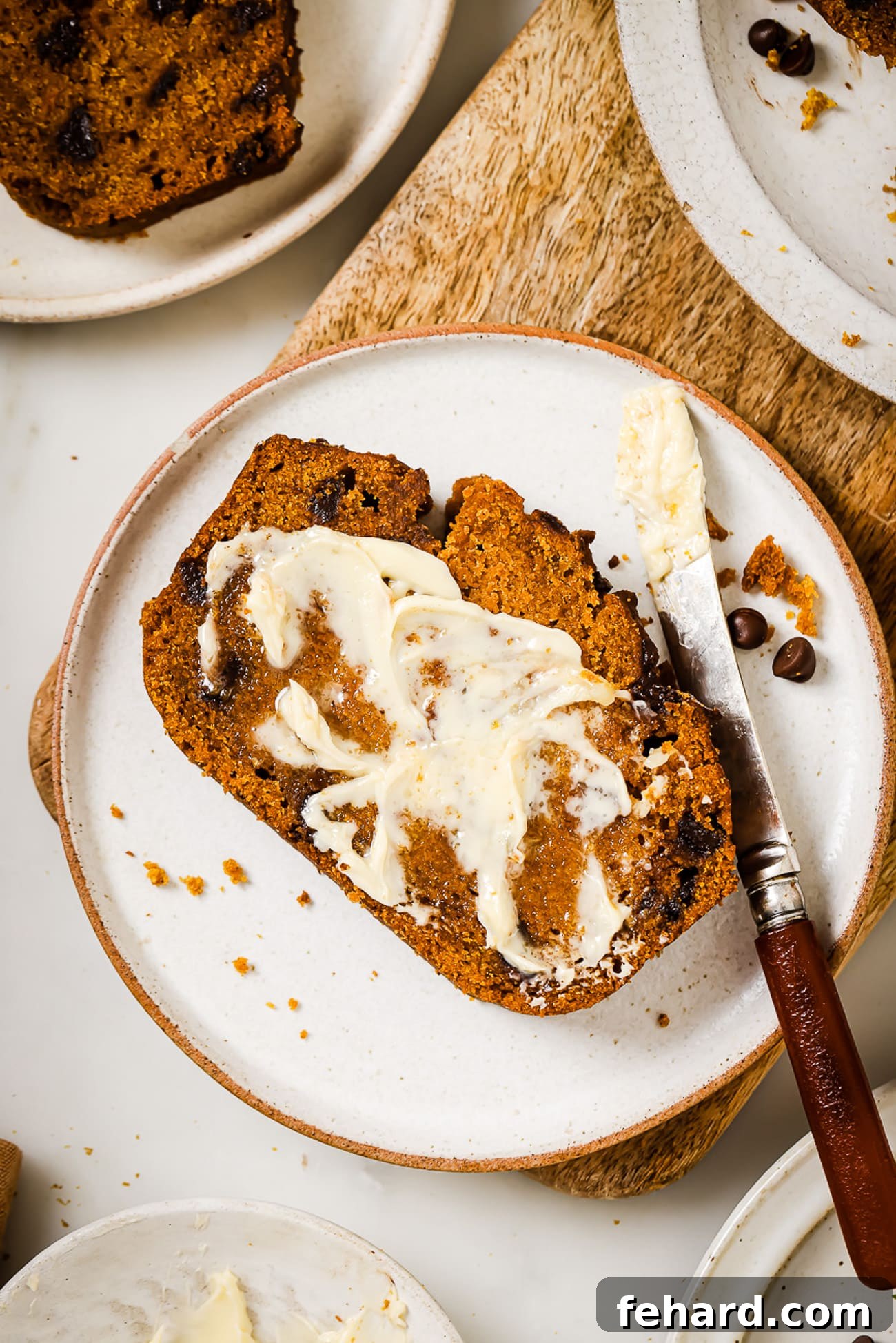 Cozy Autumn Pumpkin Chocolate Chip Loaf 9 A buttered slice of pumpkin chocolate chip bread on a white plate.