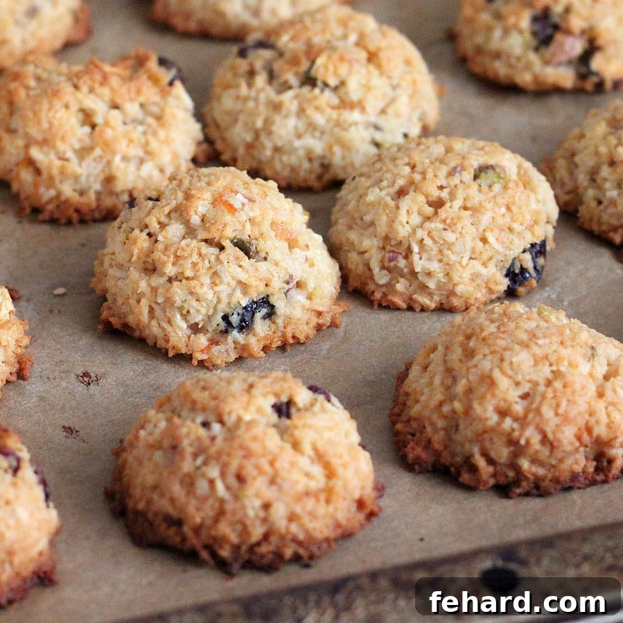 Zesty Coconut Macaroons With Cranberries and Pistachios on top of parchment paper. These colorful and chewy macaroons are a delightful vegan holiday treat.