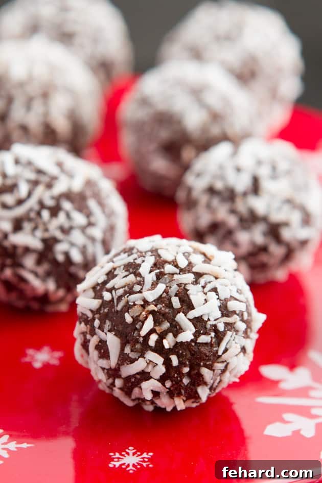 A close up of grain-free rum balls coated in shredded coconut on a red serving plate. These rich, no-bake treats are perfect for a paleo holiday.