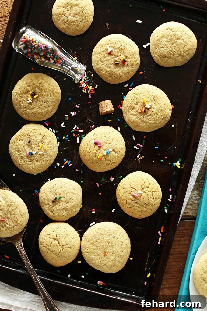 Super Soft Gluten Free Sugar Cookies topped with rainbow sprinkles on a baking sheet. These tender cookies are perfect for holiday decorating and gluten-sensitive diets.