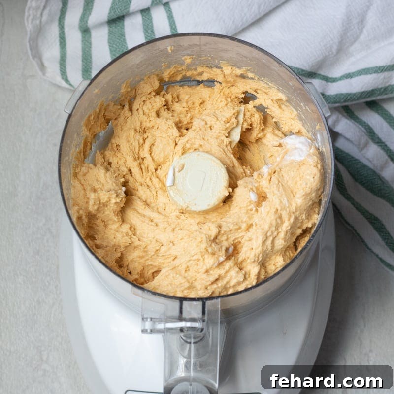 Smooth, orange-tinted sweet potato biscuit dough sitting inside a food processor bowl.
