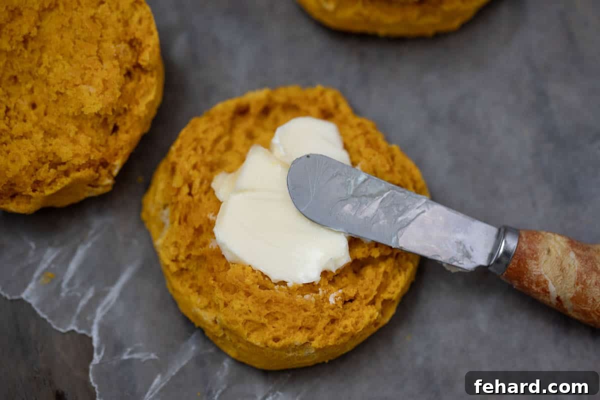 A sweet potato biscuit sliced open to reveal its moist, flaky interior, with a pat of butter melting on one half.