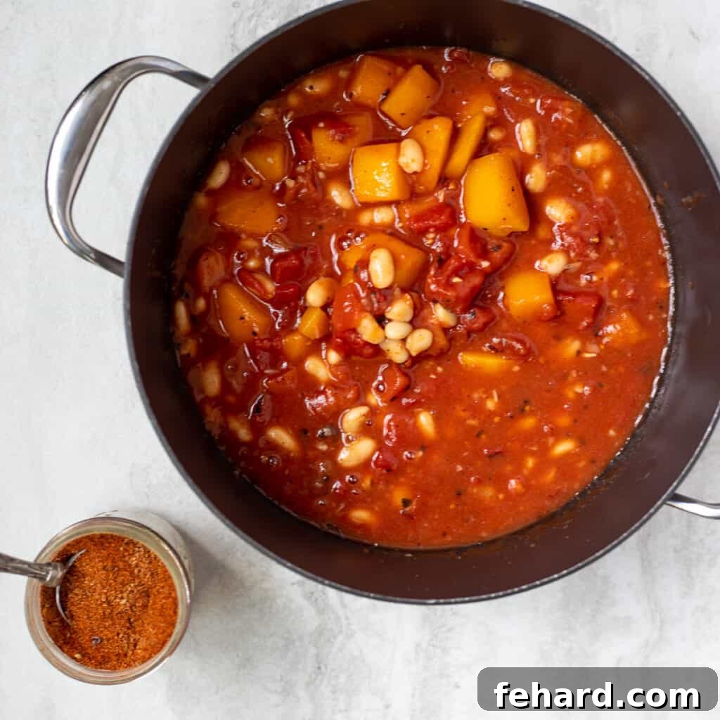Butternut Squash Chili simmering in a dutch oven on the stovetop, with chili seasoning visible nearby.