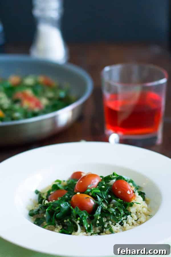 A beautifully presented bowl of warm collard quinoa salad, featuring fluffy quinoa, tender collard greens, and juicy cherry tomatoes.