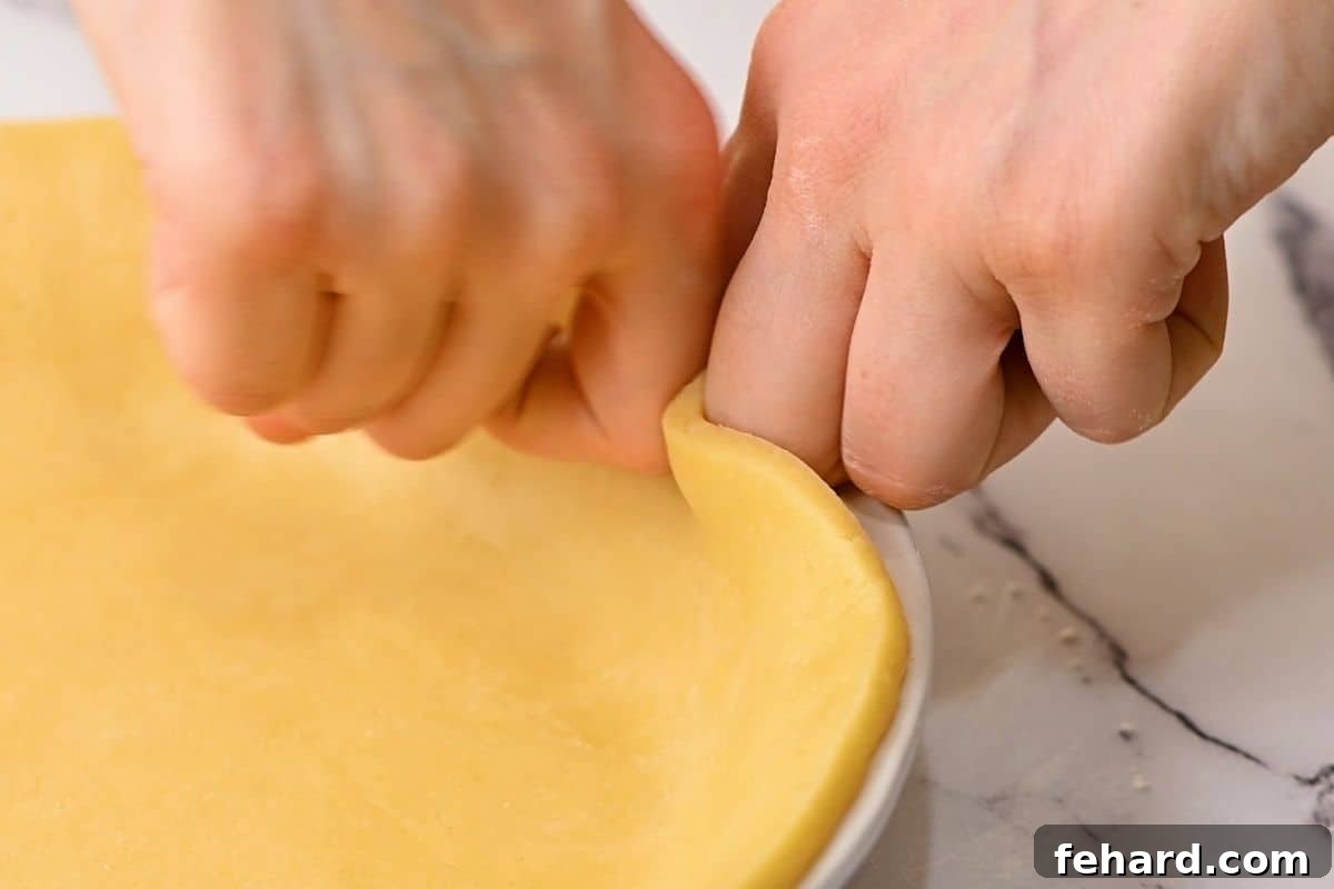Hands demonstrating the technique of fluting a pie crust edge, showing the gentle pinching and indenting motion to create decorative waves.