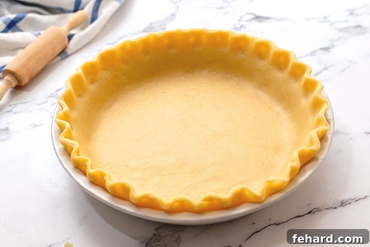 Chilled pie crust with perfectly fluted edges resting in a white ceramic pie dish, prepared and ready for its final bake or filling.