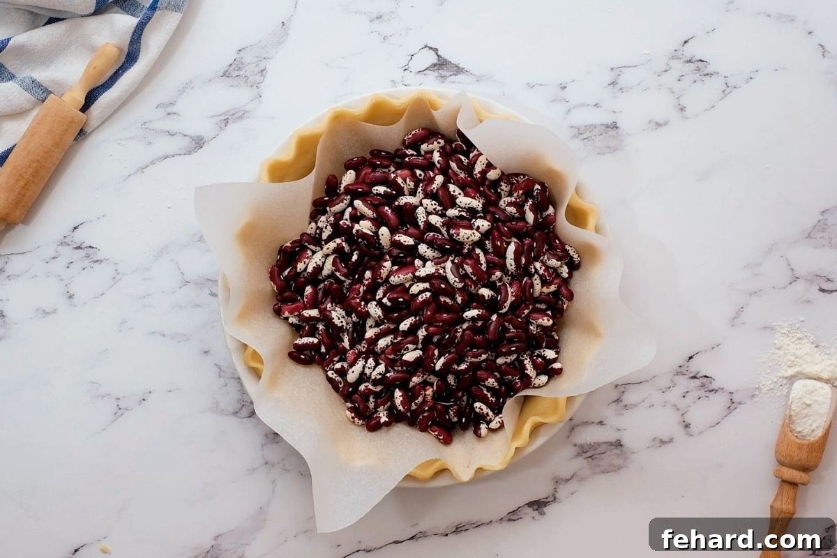 Pie crust lined with parchment paper and filled with dried beans, prepared for the blind baking process to prevent puffing and shrinking.