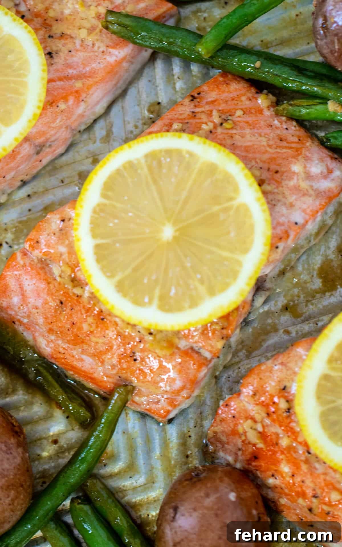 Honey Garlic Salmon Baked Close-up of golden brown honey garlic salmon on a sheet pan, surrounded by perfectly roasted green beans and potatoes.
