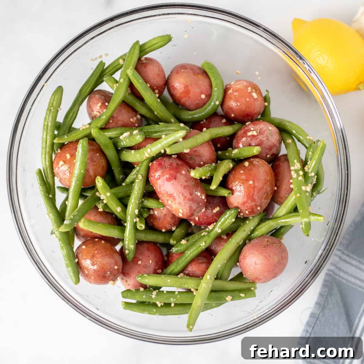 Sheet Pan Salmon Recipe Red potatoes and green beans are tossed with garlic, salt, and pepper in a clear mixing bowl, ready for roasting.