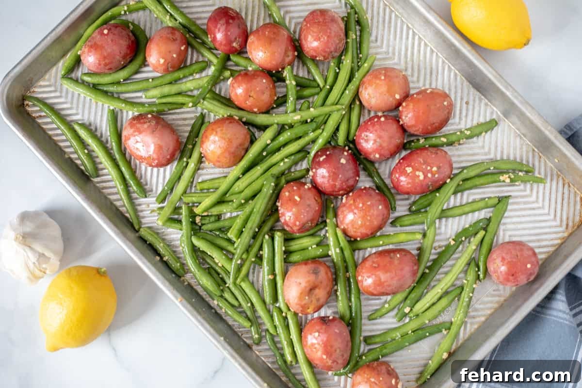 Sheet Pan Salmon Seasoned potatoes and green beans are spread evenly on a sheet pan, ready for their initial bake.