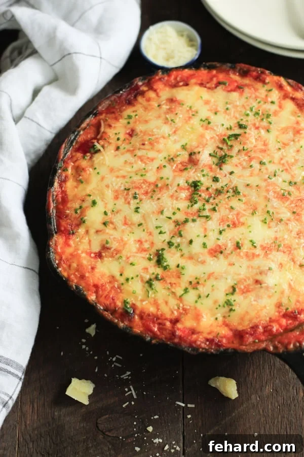 Overhead view of a cast iron skillet featuring a delicious low-carb zucchini lasagna, bubbling with cheese.