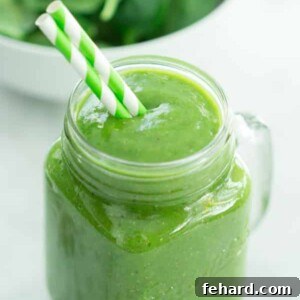 Emerald Mango Delight 2 Green Mango Green Smoothie in a mason jar with a straw, garnished with a mango slice.