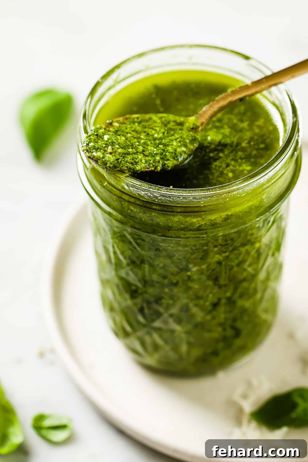 A generous spoonful of rich, homemade basil pesto delicately resting on the rim of a glass jar, showcasing its fresh texture.