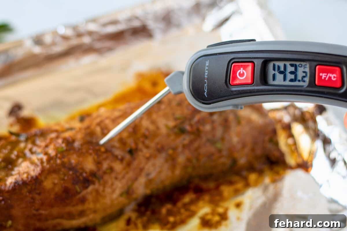 A perfectly roasted balsamic pork tenderloin on a baking sheet, with a digital meat thermometer inserted, displaying an internal temperature reading of 143 degrees Fahrenheit, indicating ideal doneness.