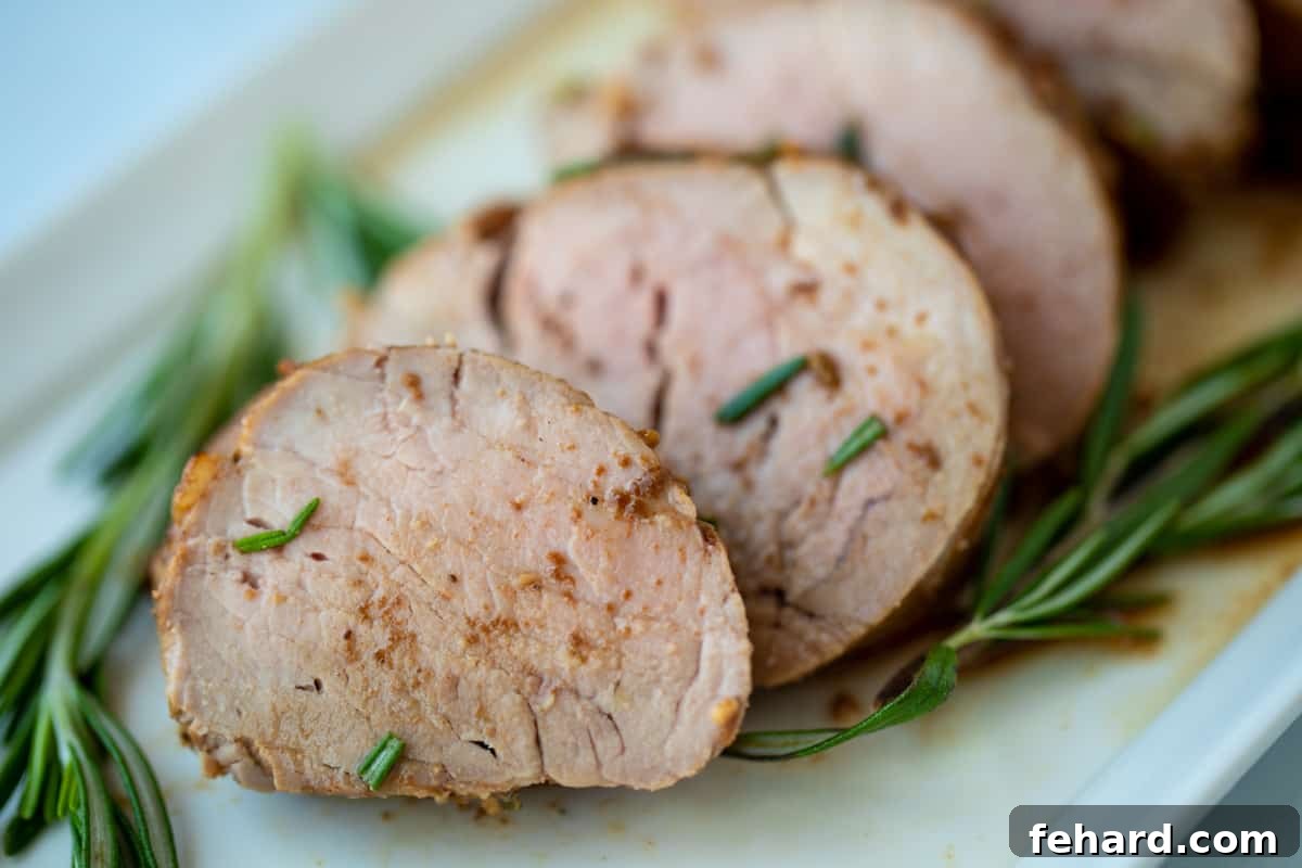 Exquisitely sliced pork tenderloin arranged on a pristine white platter, garnished with vibrant fresh rosemary sprigs. The slices reveal a succulent, juicy interior and a beautiful, caramelized crust, making for an appetizing presentation.