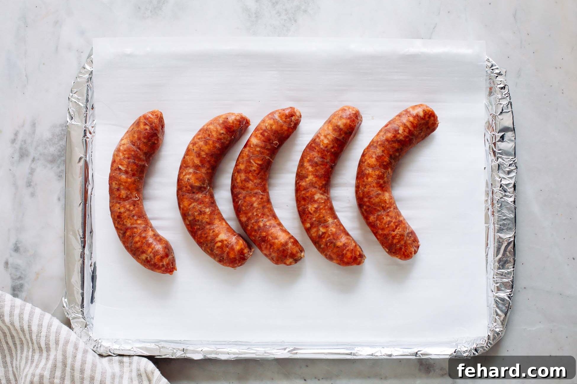 Sausage links neatly arranged on a lined baking sheet, ready for roasting.