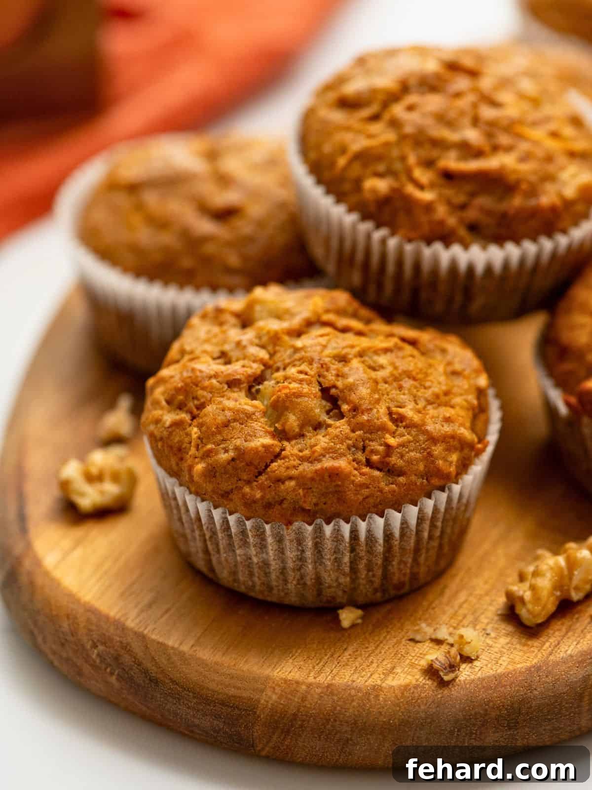 Baked carrot cake muffins in white muffin liners, garnished with fresh carrots, pineapple, and walnuts.