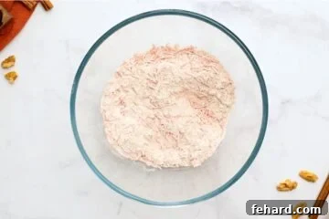 Flour and spices mixed together in clear mixing bowl with grated carrots and nuts.