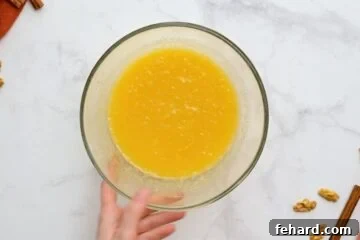 Applesauce, eggs, oil, honey, and crushed pineapple whisked together in mixing bowl for carrot cake muffins.
