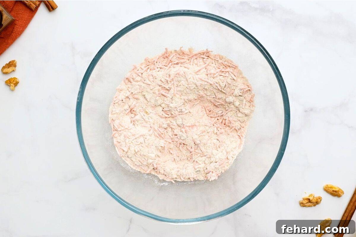 Flour and spices combined with shredded carrots and chopped walnuts in a mixing bowl.