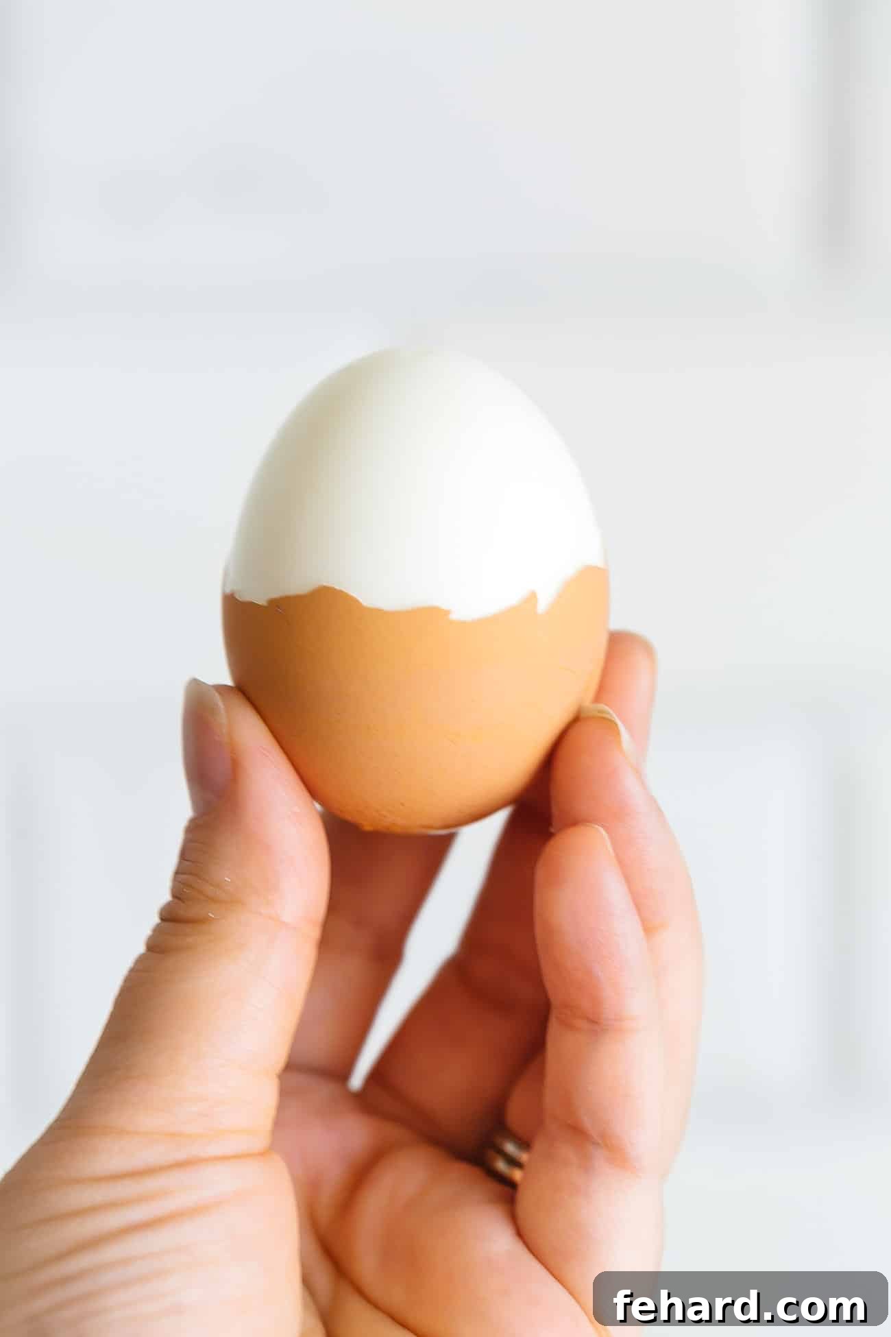 A hand holding a half-peeled hard boiled egg, showcasing its easy peel.