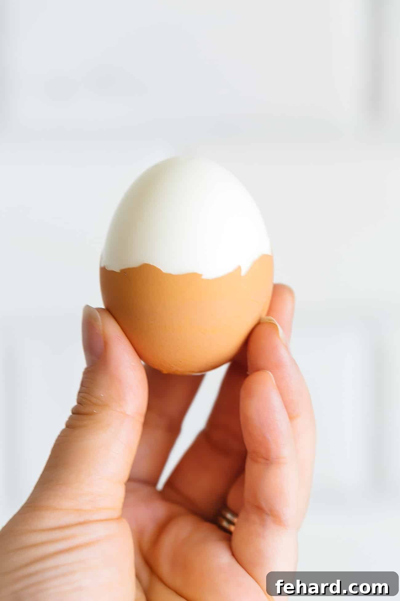 A hand holding a half peeled hard boiled egg.
