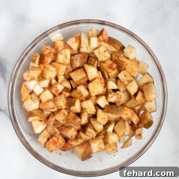 Crispy Air Fryer Potato Bites 4 Cubed potatoes with dried seasonings in glass mixing bowl.