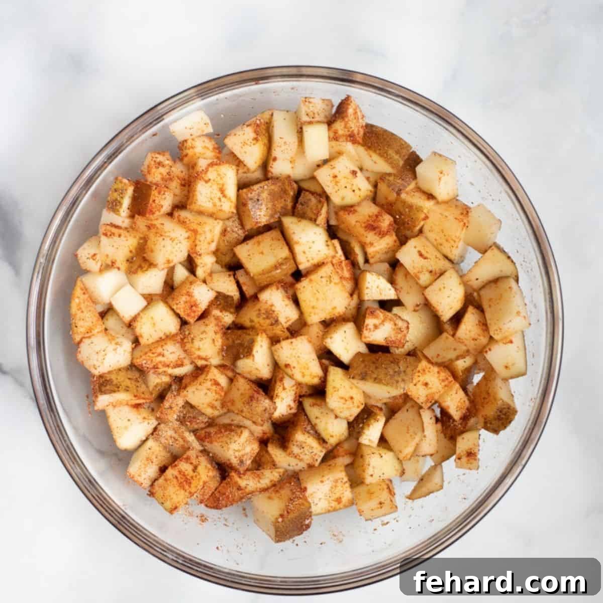Seasoning Potatoes for Air Frying Close-up of cubed potatoes in a clear glass mixing bowl, generously coated with dried seasonings, ready for the air fryer.