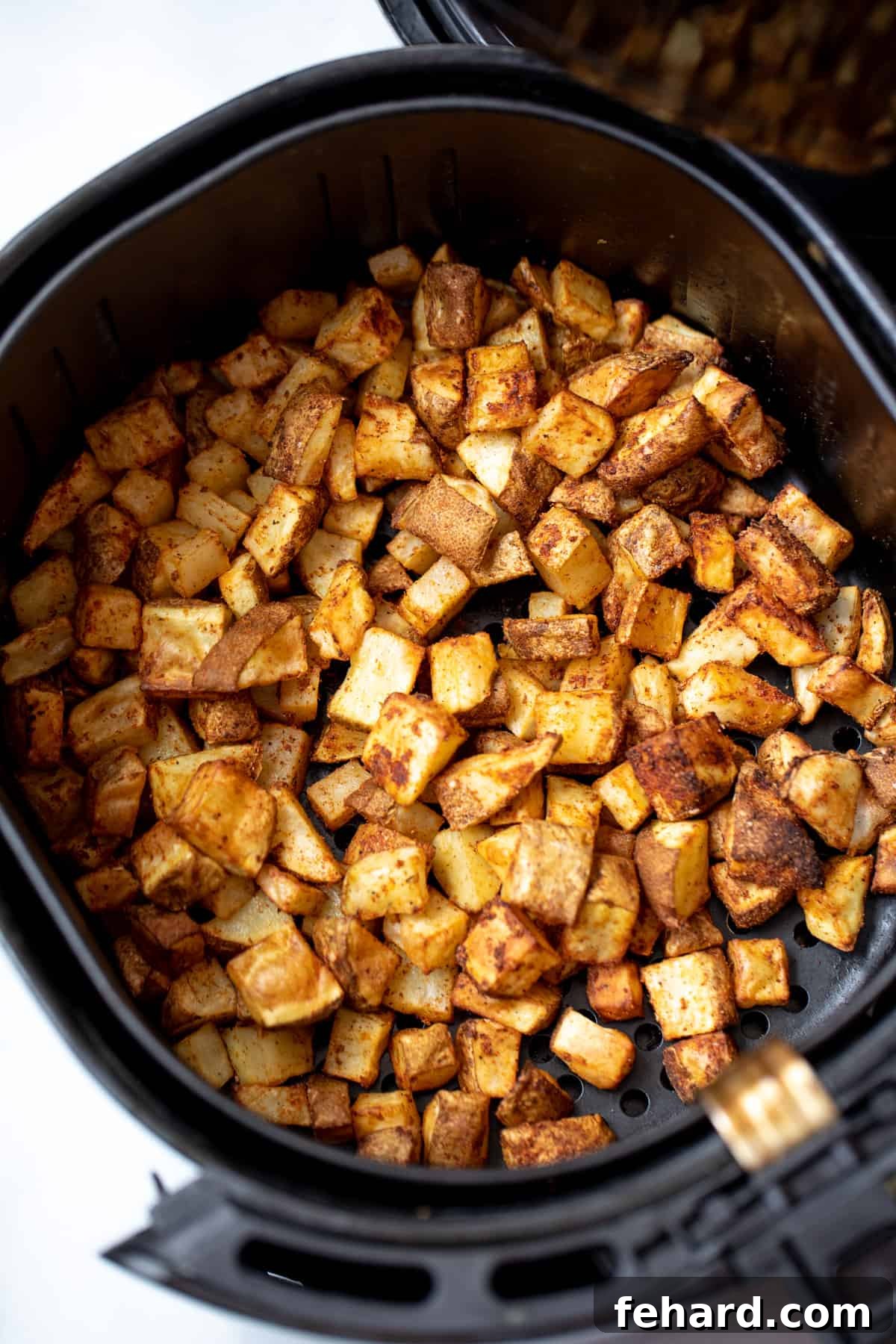 Finished Air Fried Diced Potatoes A close-up view of perfectly air-fried, golden-brown potato cubes inside an air fryer basket, showcasing their crispy texture.