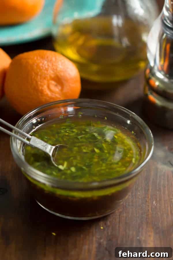 A close-up overhead shot of the Clementine Salad Dressing, showcasing the finely chopped fresh parsley and specks of clementine zest mixed into the golden liquid.