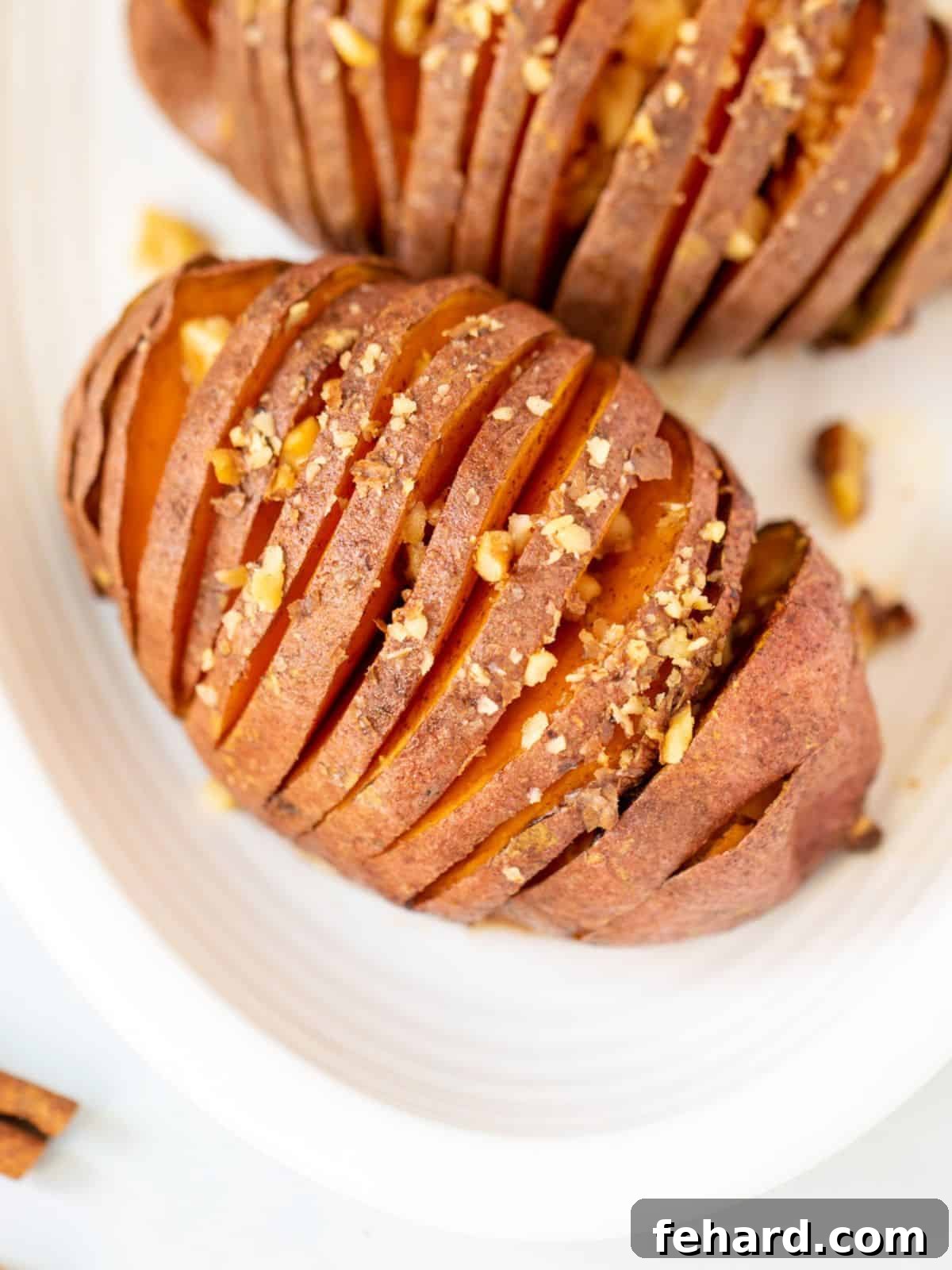 Maple Glazed Hasselback Sweet Potatoes Top down view of maple-glazed hasselback sweet potato on white platter, garnished with toasted nuts.