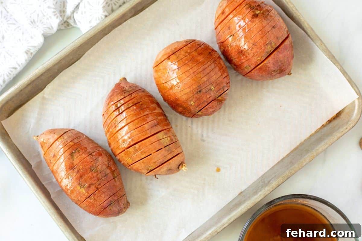 Hasselback Sweet Potato Baking Glazed, sliced sweet potatoes on a baking tray lined with parchment paper, before the second glaze and nuts.