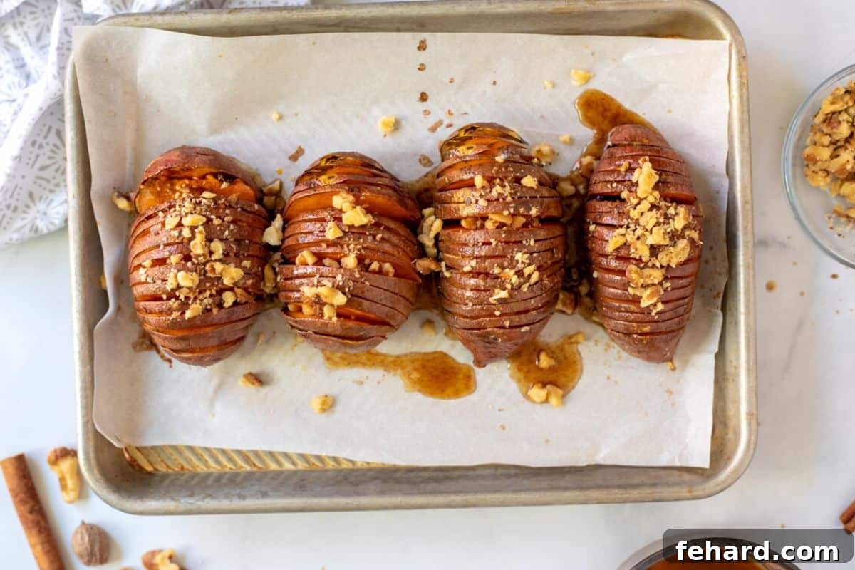 Finished Glazed Sweet Potatoes Hasselback sweet potatoes on a baking tray after being glazed and topped with nuts, ready to serve.