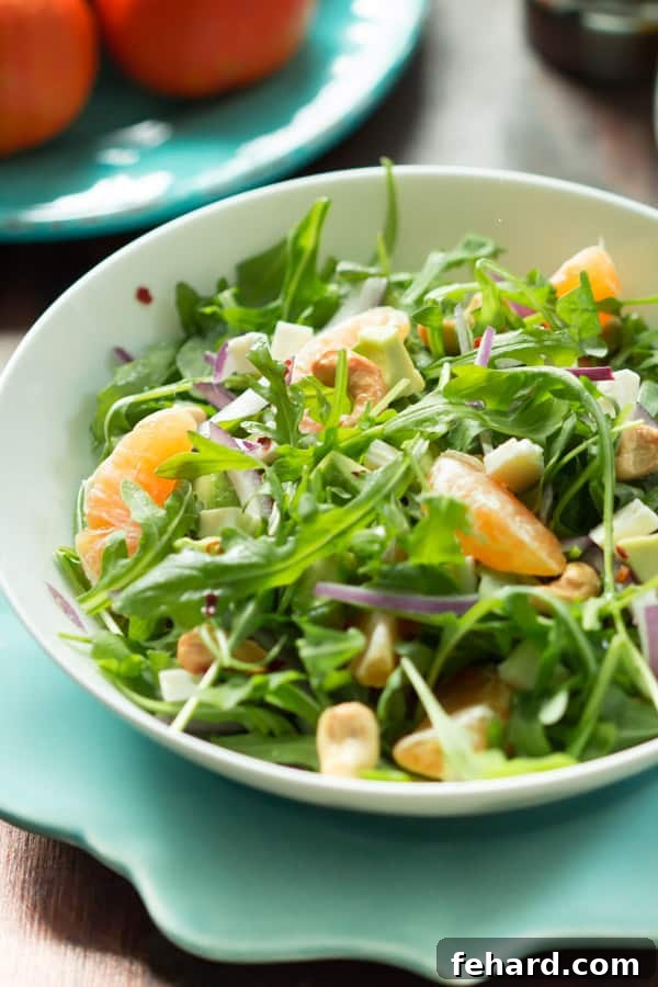 Clementine Arugula Salad Fresh Ingredients Ingredients for Clementine Arugula Salad laid out on a wooden board, featuring clementines, fresh arugula, avocado, red onion, and cashews.