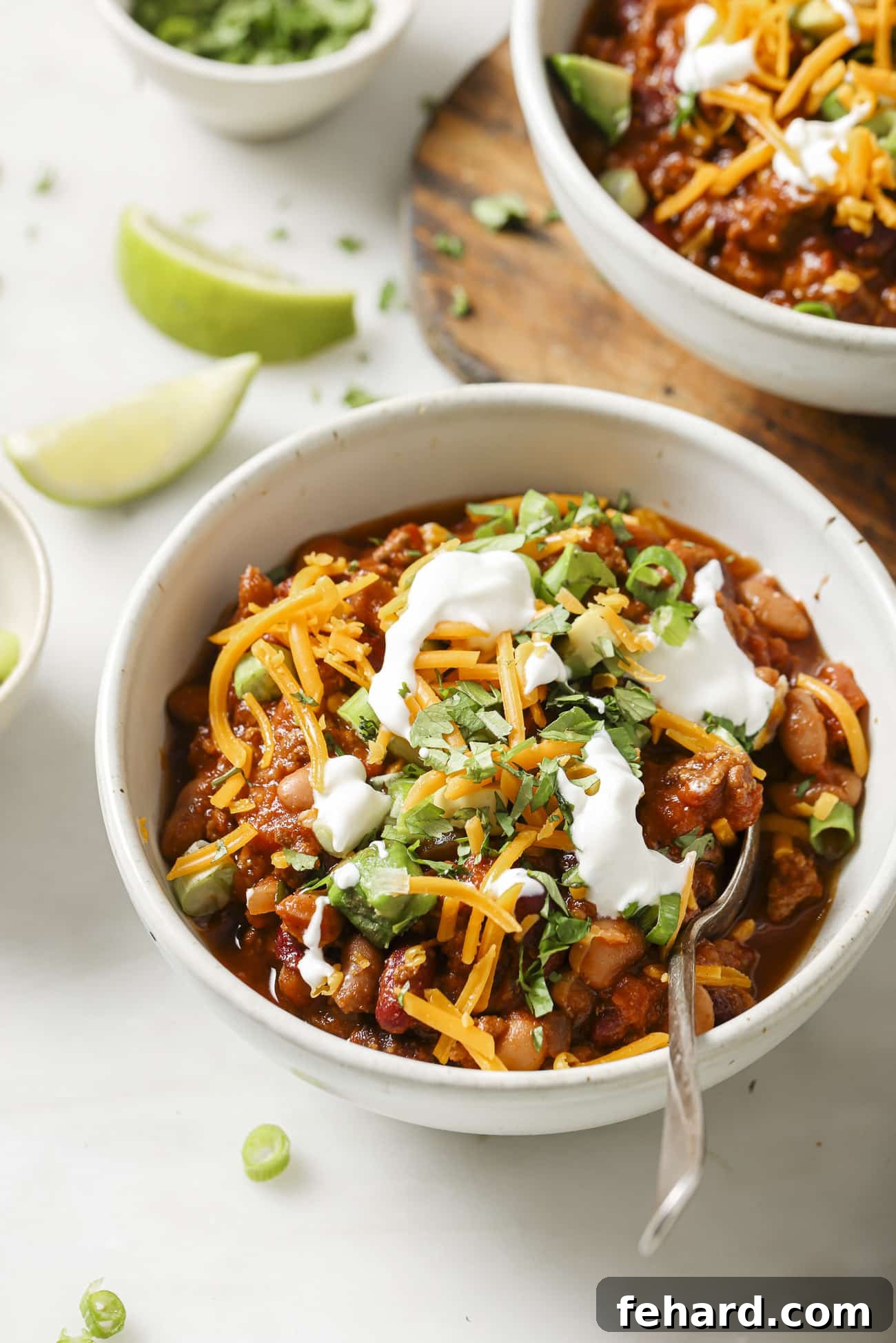 Set It and Forget It Chili 9 A beautifully presented bowl of slow cooker chili, richly garnished with fresh green onions, sour cream, and shredded cheddar cheese, ready for enjoyment.