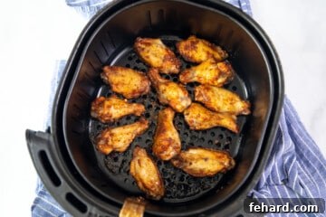 Crispy, golden-brown chicken wings perfectly arranged in an air fryer basket, steam rising, indicating they are hot and ready.
